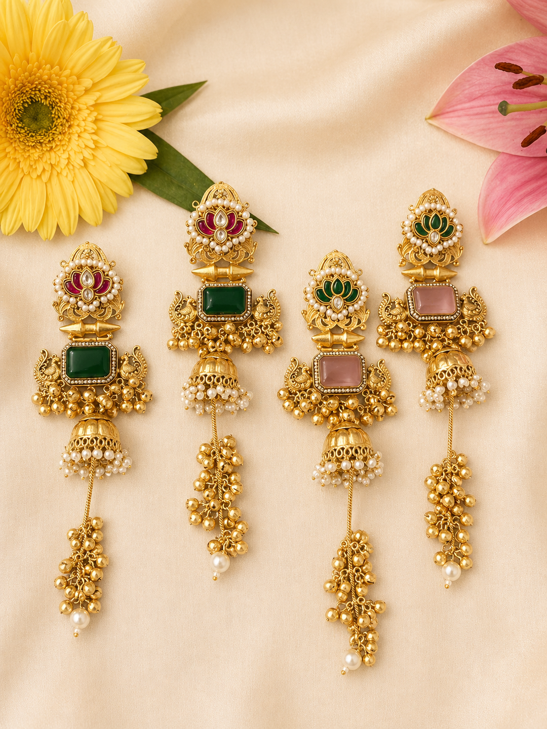 two pairs of gold earrings with gemstones on a beige background with flowers.