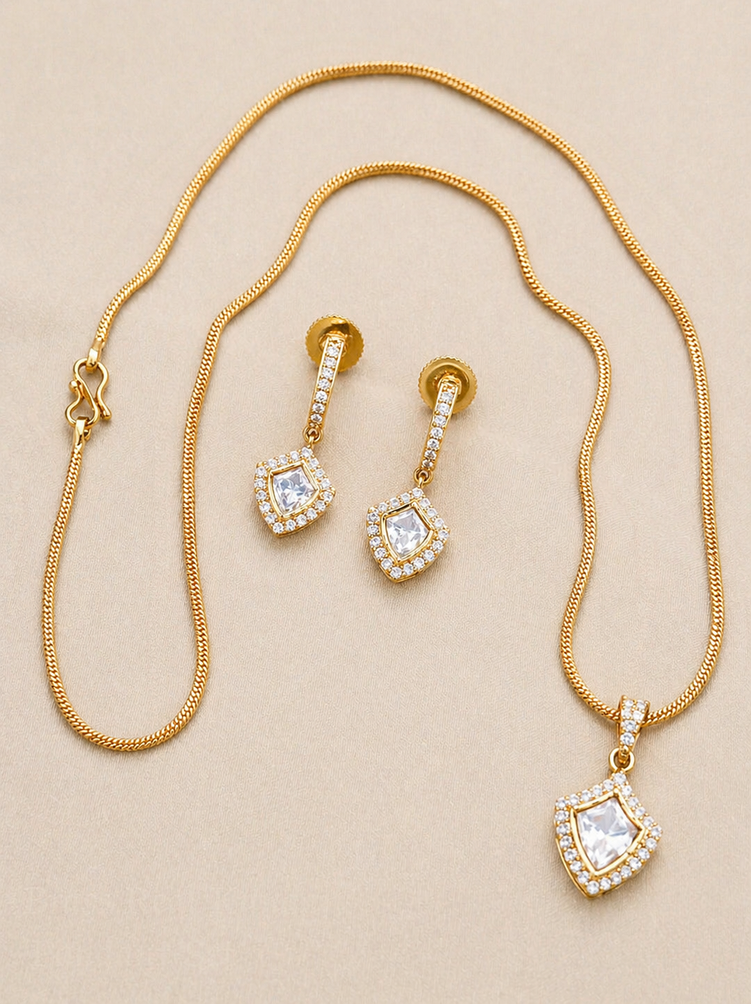 Gold necklace and earrings set on a beige background