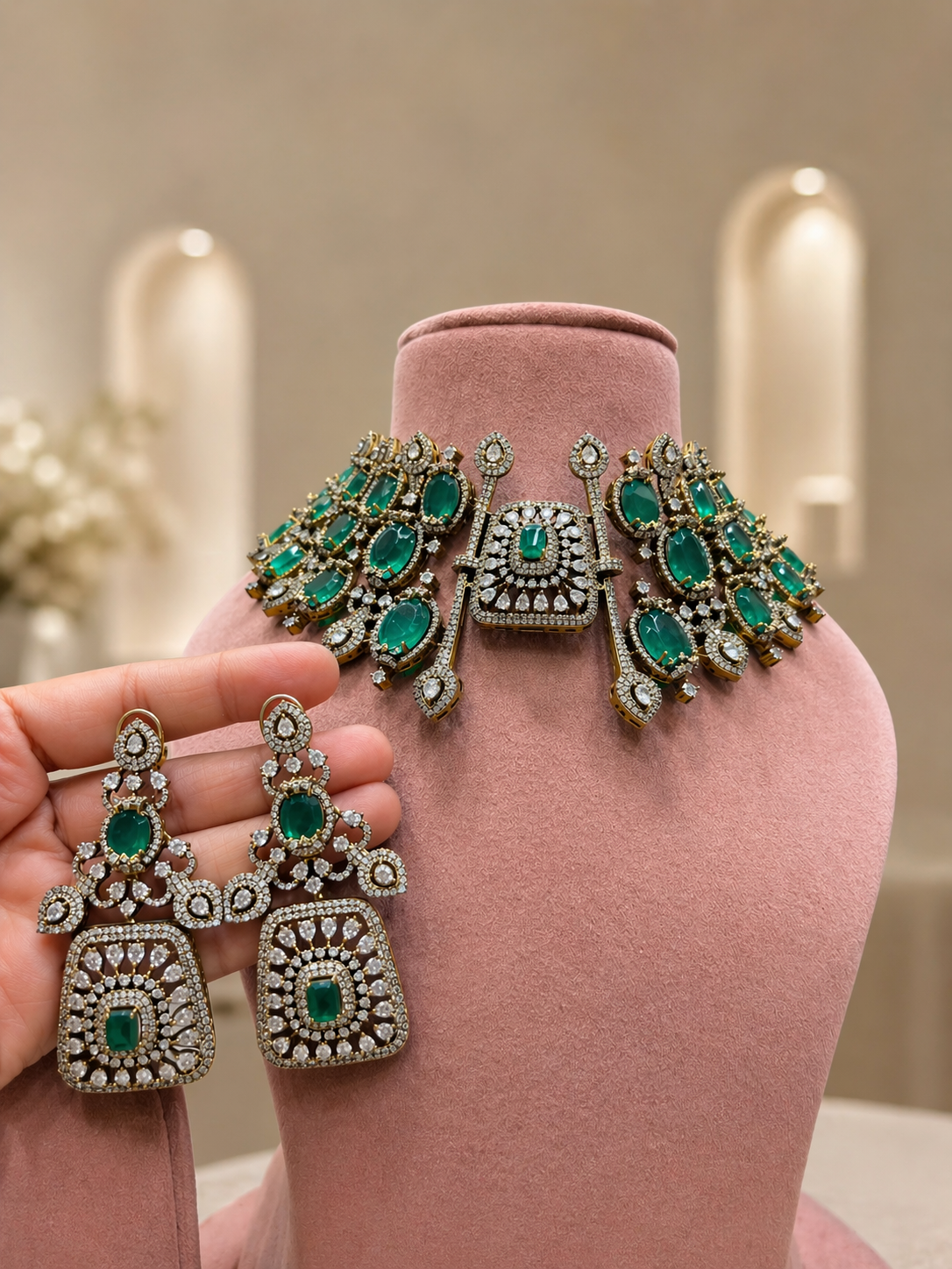 Ornate earrings with green gemstones held by a hand on a pink stand.