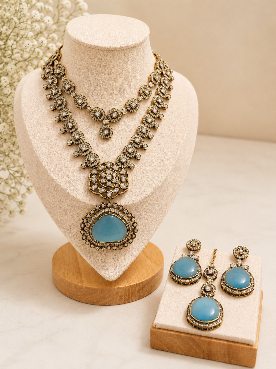 oft aqua-toned stones framed with intricate antique-inspired detailing and luminous crystal accents. The layered silhouette creates a refined statement while maintaining a timeless vintage charm. Complete with matching earrings and maang tikka, this set is perfect for receptions, festive evenings, and elevated occasion styling.