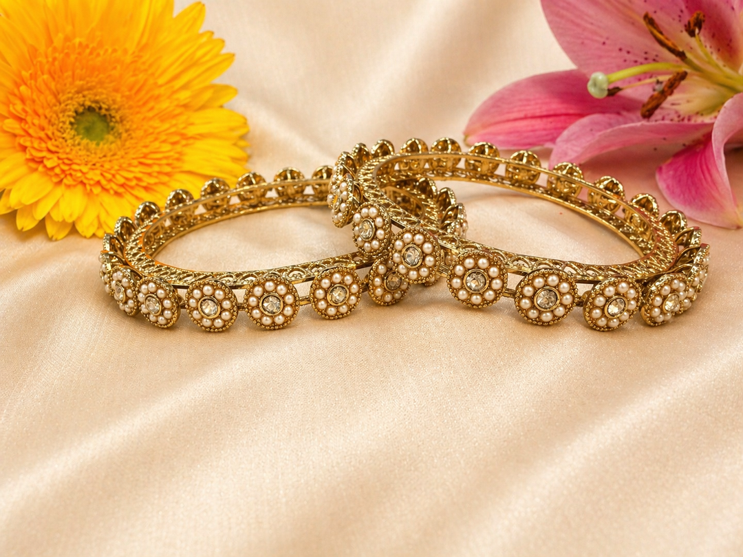 Pair of gold bangles with floral decorations on a beige fabric background