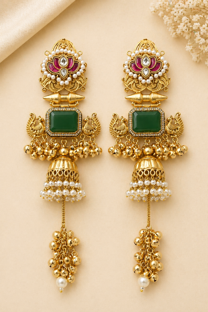 Ornate gold earrings with green stones and pearl accents on a beige background