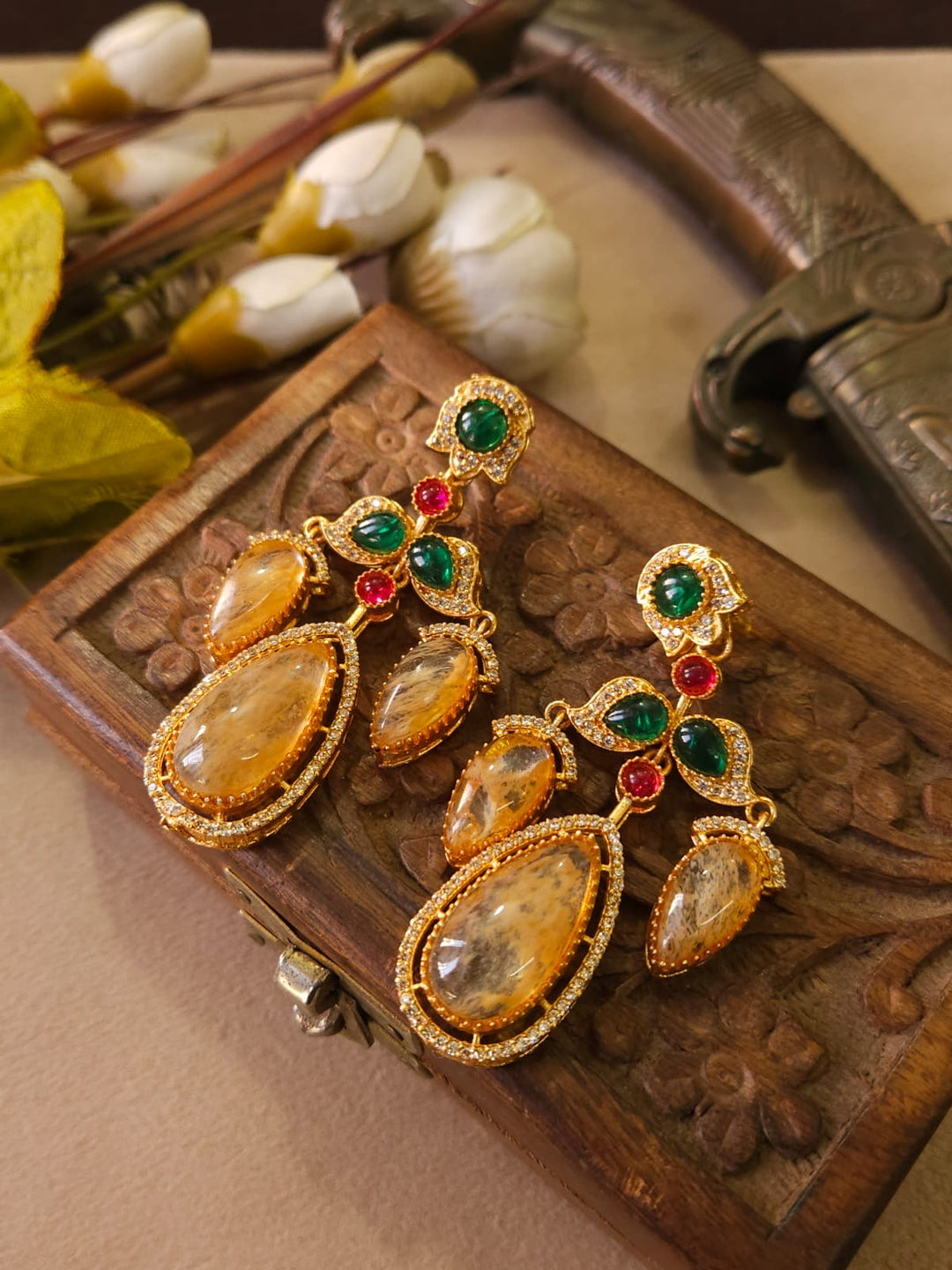 Gold earrings with gemstones on a decorative wooden box