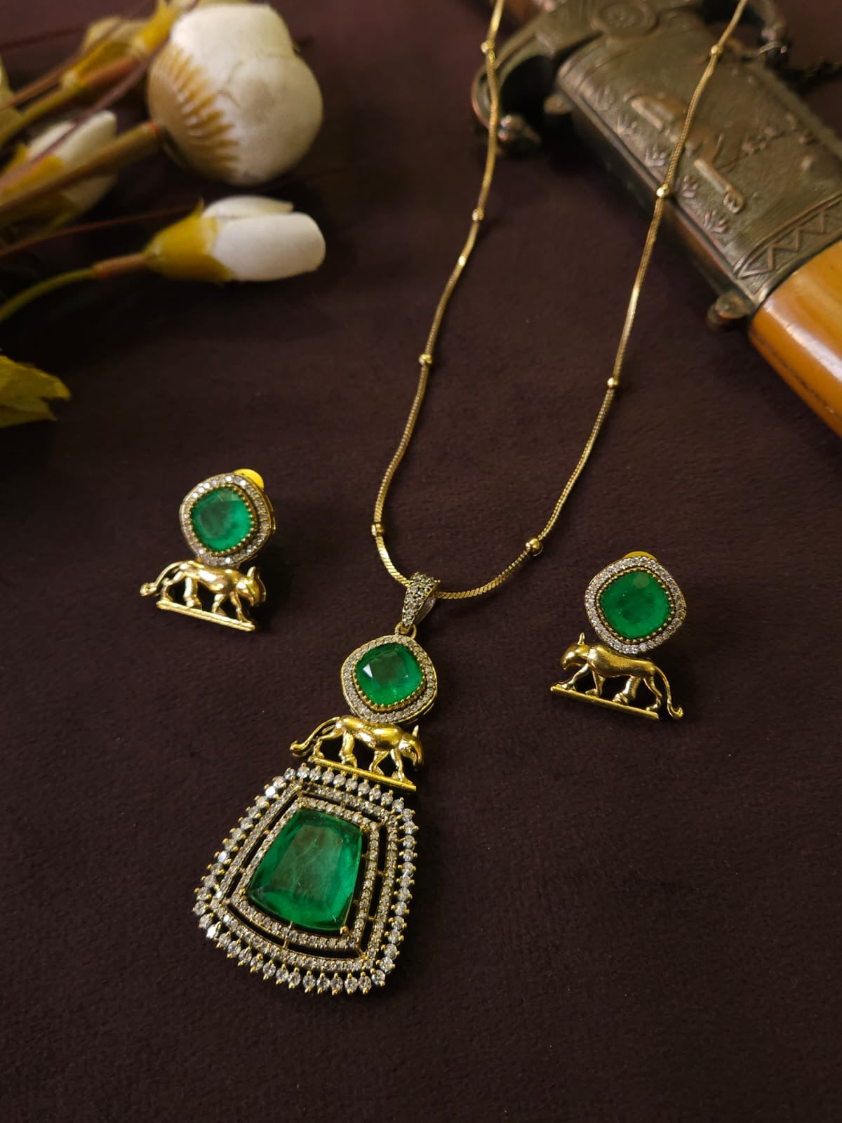Jewelry set with emerald green stones and gold accents on a dark surface.