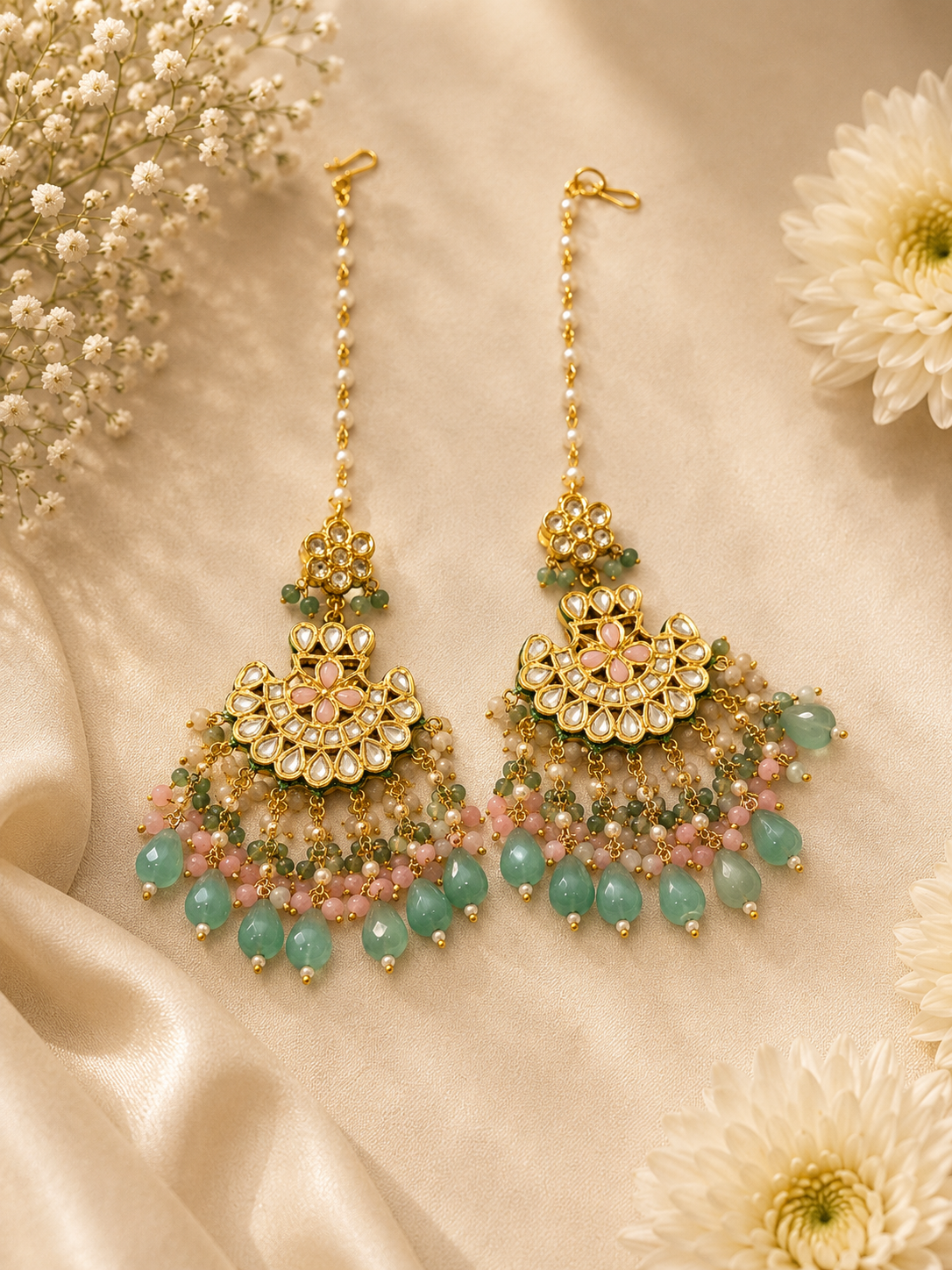 Ornate gold and gemstone earrings on a beige fabric background with flowers.