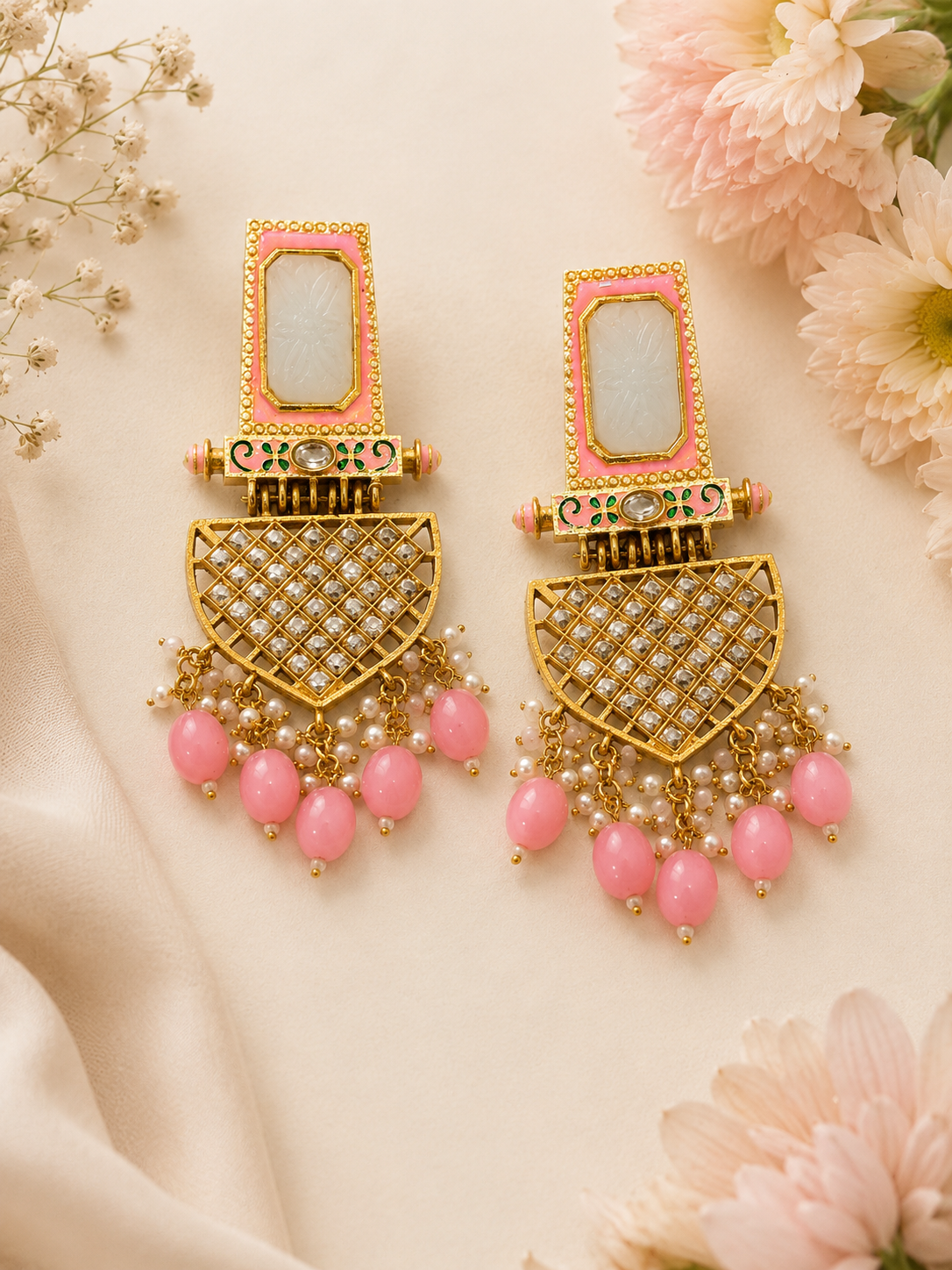 Ornate gold earrings with pink beads on a floral background