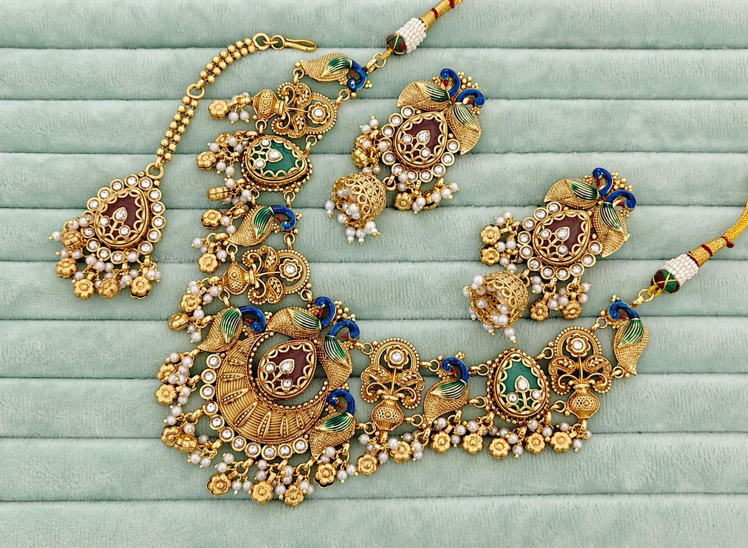Ornate gold necklace with gemstones on a light green fabric background