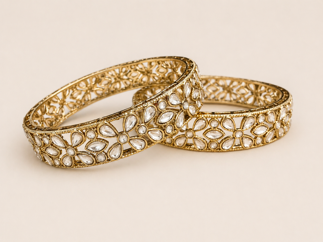 Gold-toned bangles featuring a delicate floral pattern with clear stones arranged in an intricate, openwork design.
