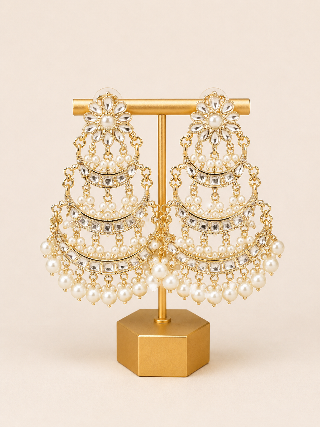 Pair of pearl and gold chandelier earrings on a gold stand against a beige background