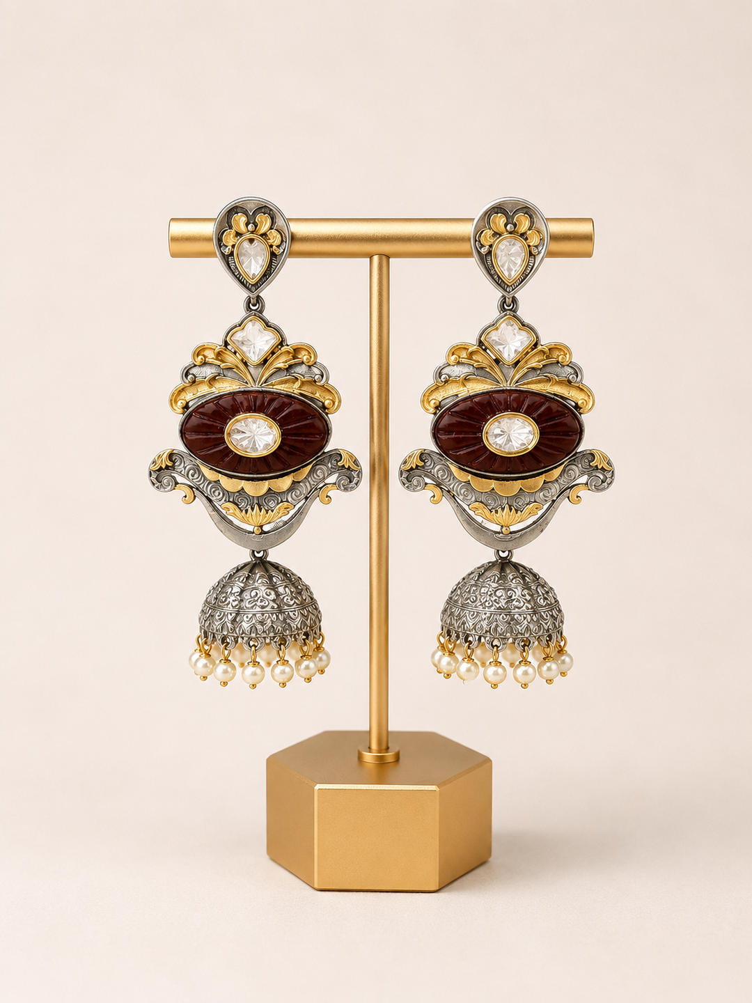 Ornate earrings on a gold stand against a beige background