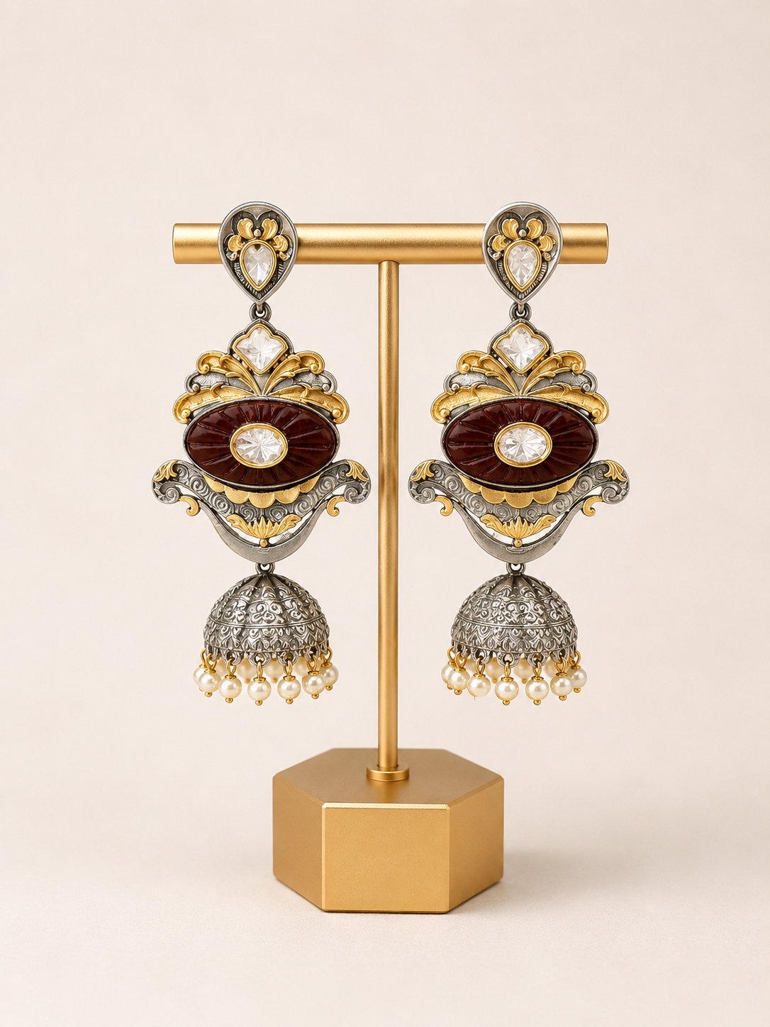 Ornate earrings on a gold stand against a beige background