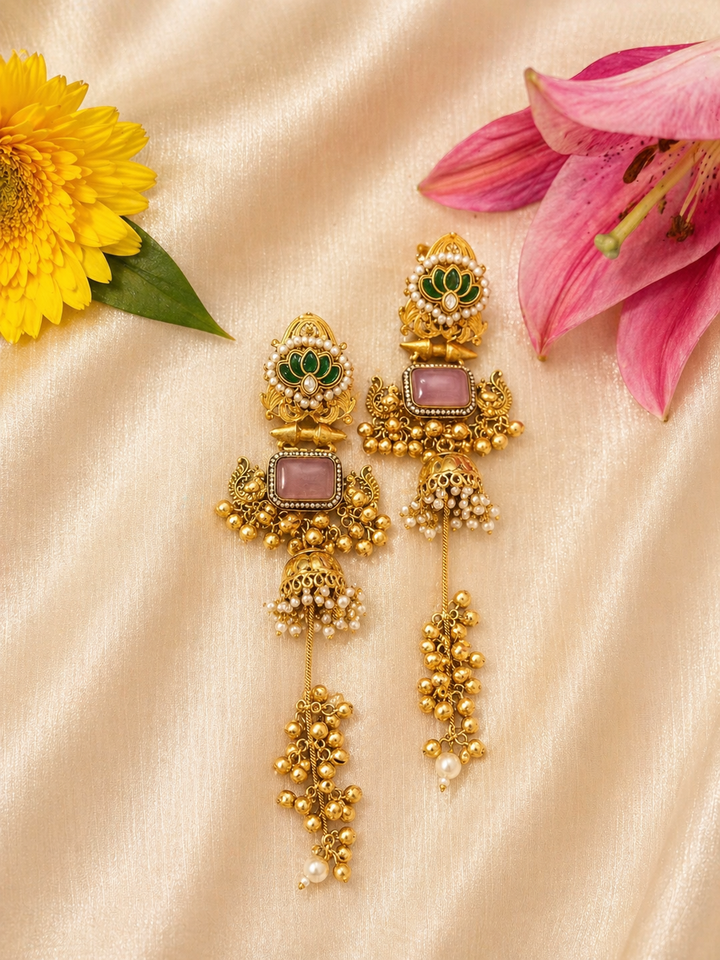 Gold earrings with gemstones on a beige fabric background with flowers.