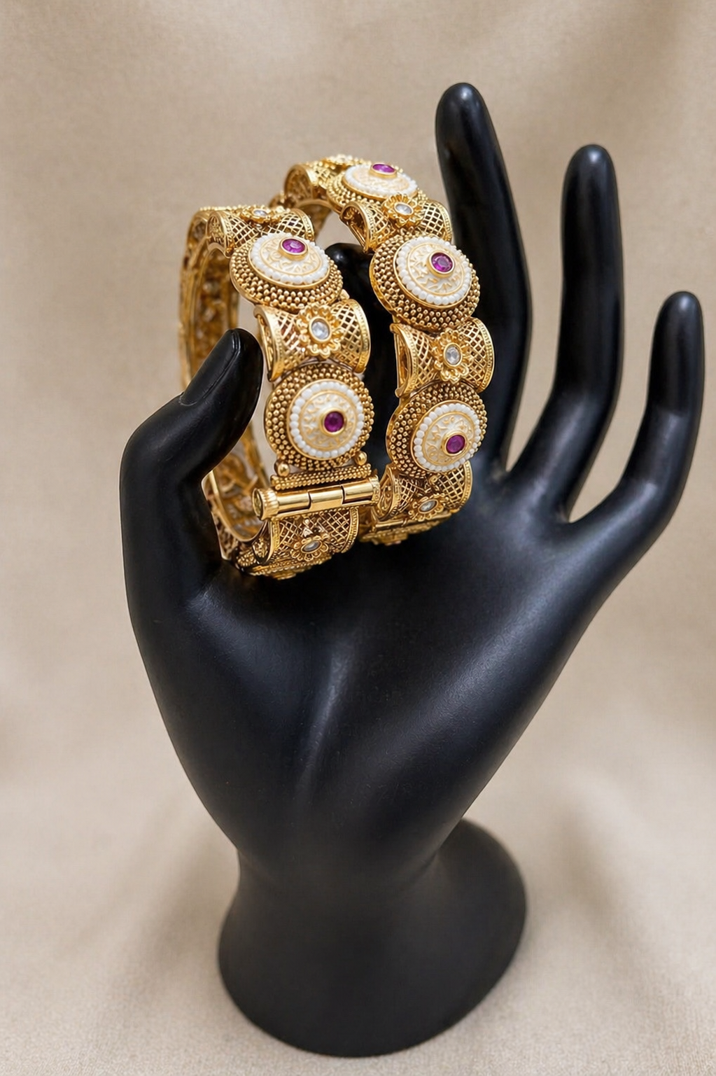 Gold bracelets with gemstones on a black mannequin hand against a beige background