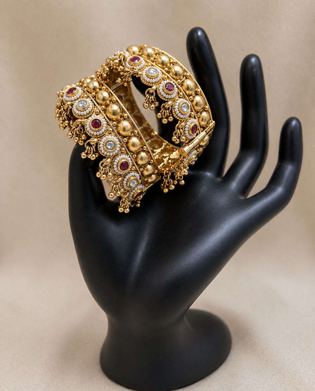 Gold bracelet with gemstones on a black mannequin hand against a beige background