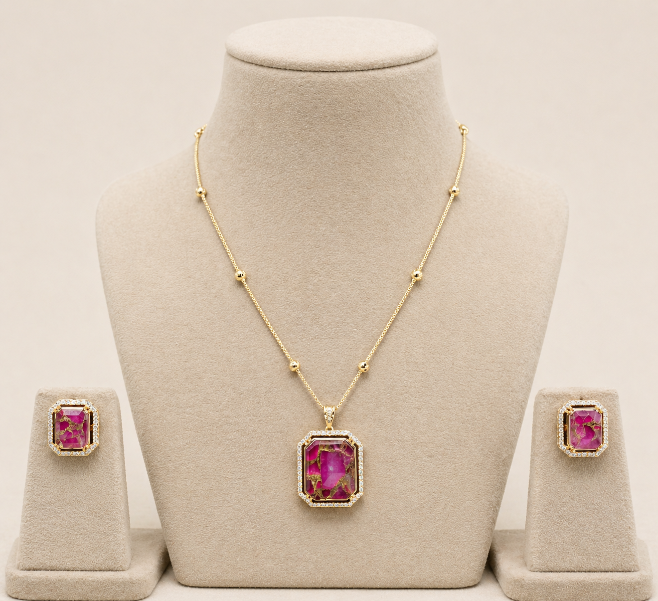 Gold necklace with pink gemstones on a mannequin bust, accompanied by matching earrings.