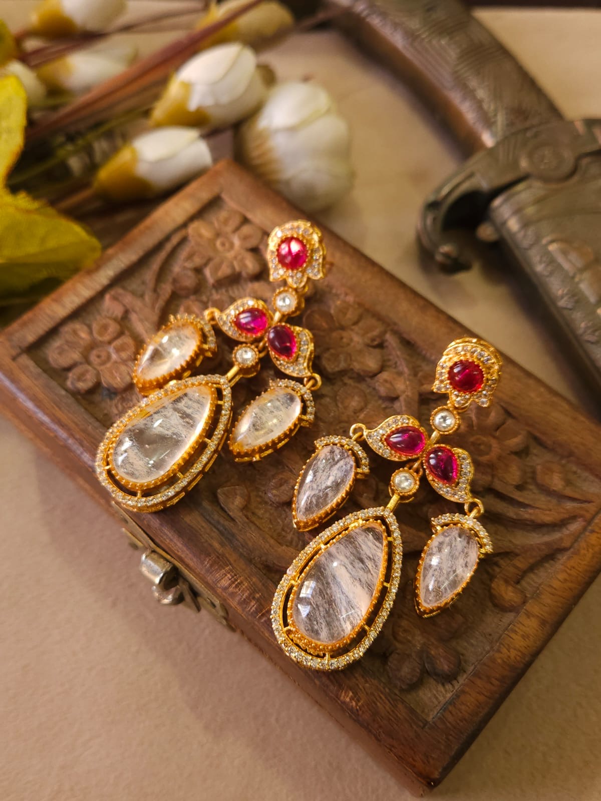Ornate earrings with red and clear stones on a wooden box