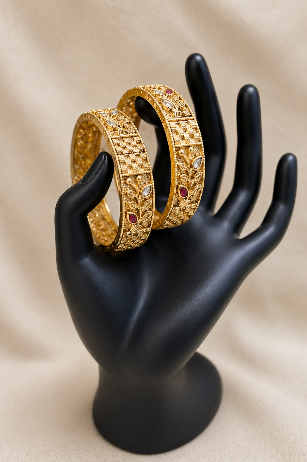 Gold textured bangles with intricate detailing and ruby accents on display stand