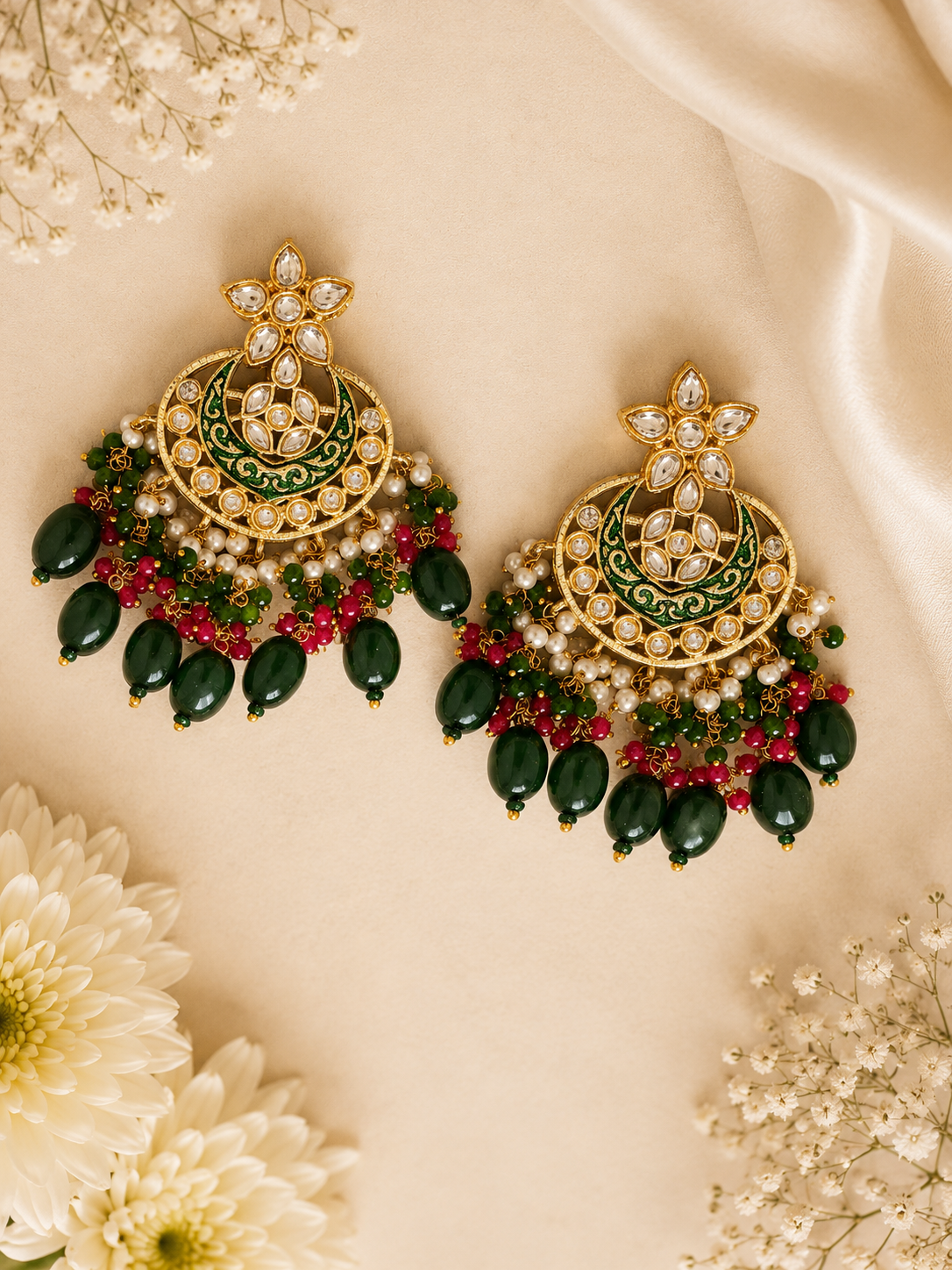 Pair of ornate earrings with green, red, and gold details on a beige background with flowers.