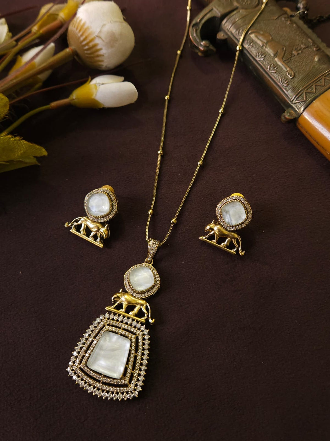 Gold necklace with pendant and matching earrings on a dark surface
