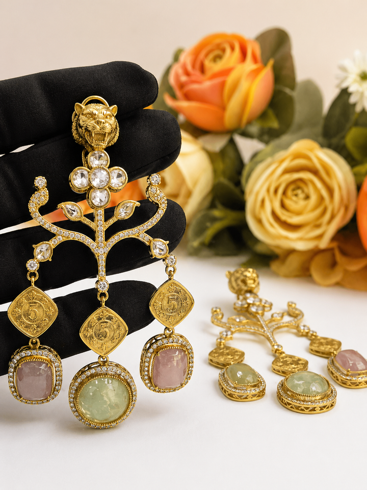 Gold earrings with gemstones on a black stand, with flowers in the background